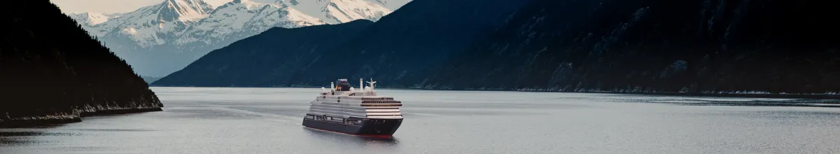 Das luxuriöse EXPLORA Schiff fährt anmutig durch einen Fjord in Alaska, der von hohen Klippen eigerahmt ist.