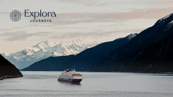 Eines der luxuriösen EXPLORA Schiffe fährt in der Dämmerung durch einen Fjord in Alaska.