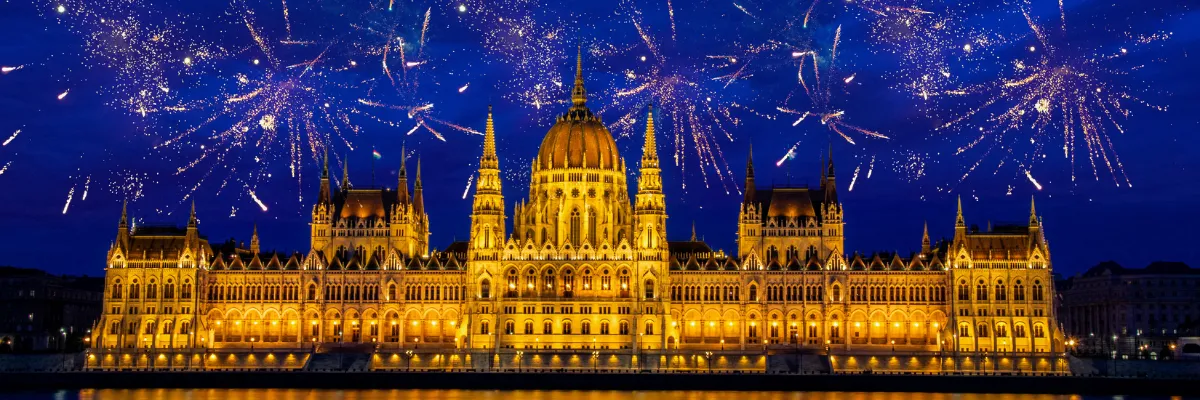 1AVista Silvester-Kreuzfahrt 2026 Das Budapester Parlament wird in der Nacht ausgeleuchtet. Über dem Gebäude explodieren viele kleine Feuerwerkskörper.