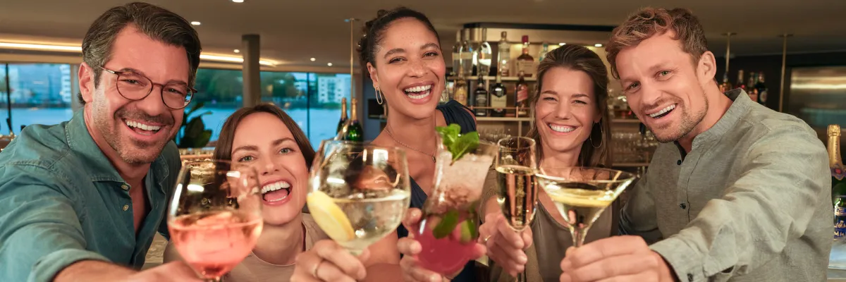 A-ROSA Silvester-Flusskreuzfahrt 2026 Vier Personen feiern ausgelassen Silvester auf einem Schiff von A-ROSA. Alle haben ein anderes Getränk.
