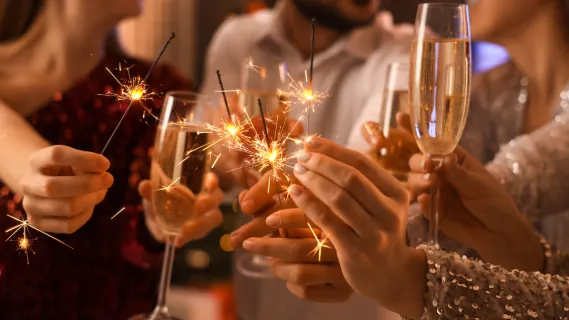 Silvesterreise auf dem Fluss 2026 Eine Gruppe Personen in festlichen Klamotten stoßen mit Champagner und Wunderkerzen auf das neue Jahr an.