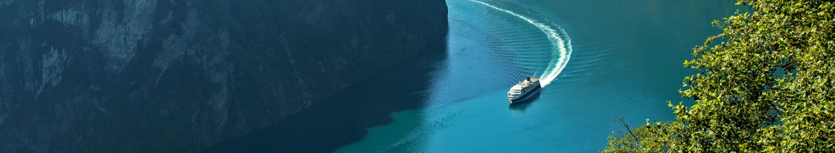 Zwischen zwei imposanten Klippen fließt ein norwegischer Fjord. Auf dem Wasser zieht ein Kreuzfahrtschiff seine Runde.