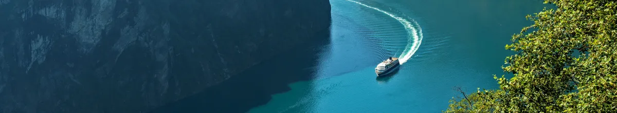 Zwischen zwei imposanten Klippen fließt ein norwegischer Fjord. Auf dem Wasser zieht ein Kreuzfahrtschiff seine Runde.