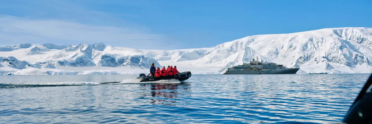 All Inclusive Kreuzfahrt: Luxusreise Ein kleines Zodiac von Silversea fährt mit ein paar Personen in roten Parkas zurück zum Expeditionsschiff in der Arktis.