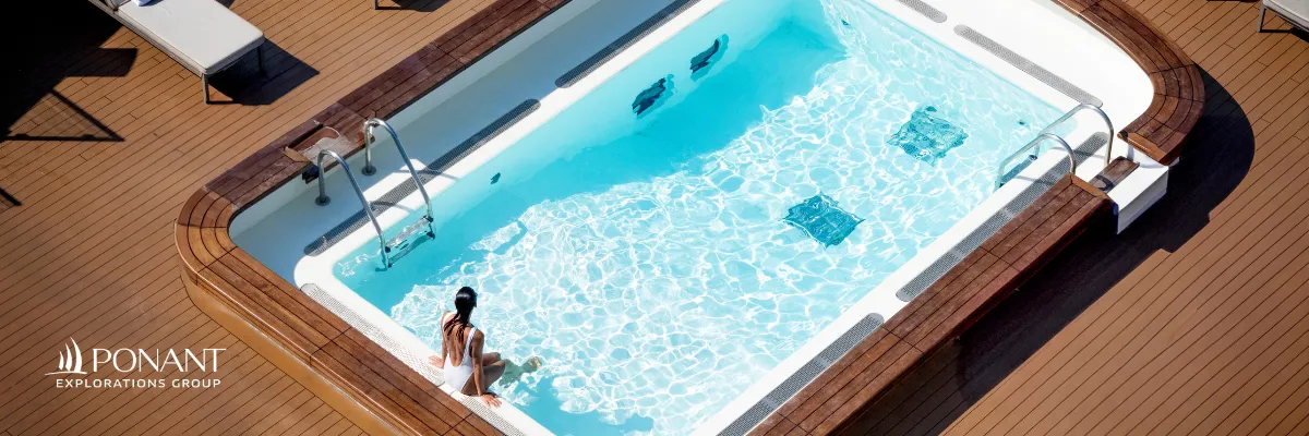 Eine Frau sitzt alleine an einem luxuriösen Pool auf einem Schiff von Ponant.