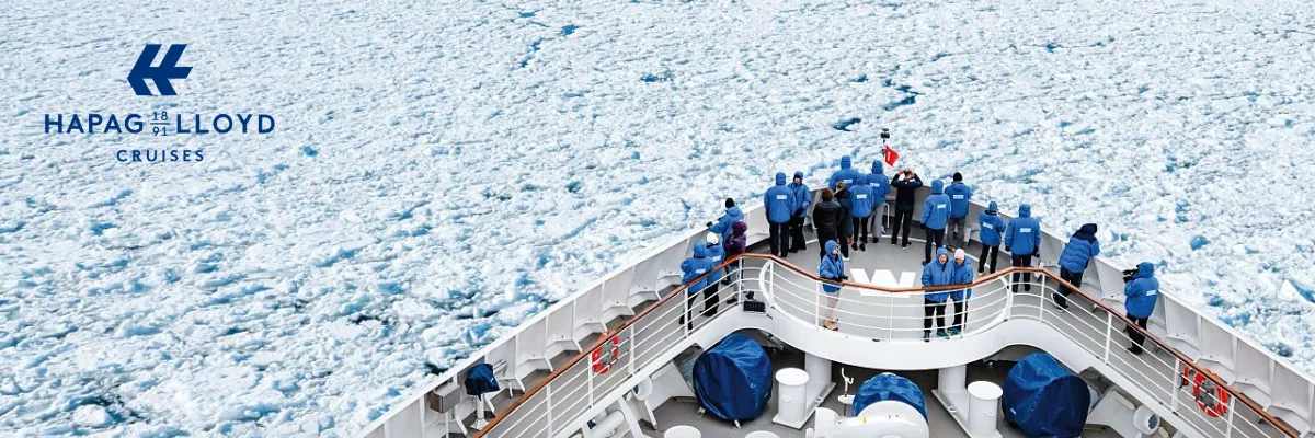 Expeditionskreuzfahrten mit Hapag-Lloyd Cruises Eine Gruppe Personen in blauen Parkas von Hapag-Lloyd stehen am Bug eines HANSEATIC Schiffs und schauen auf die Eislandschaft der Antarktis.