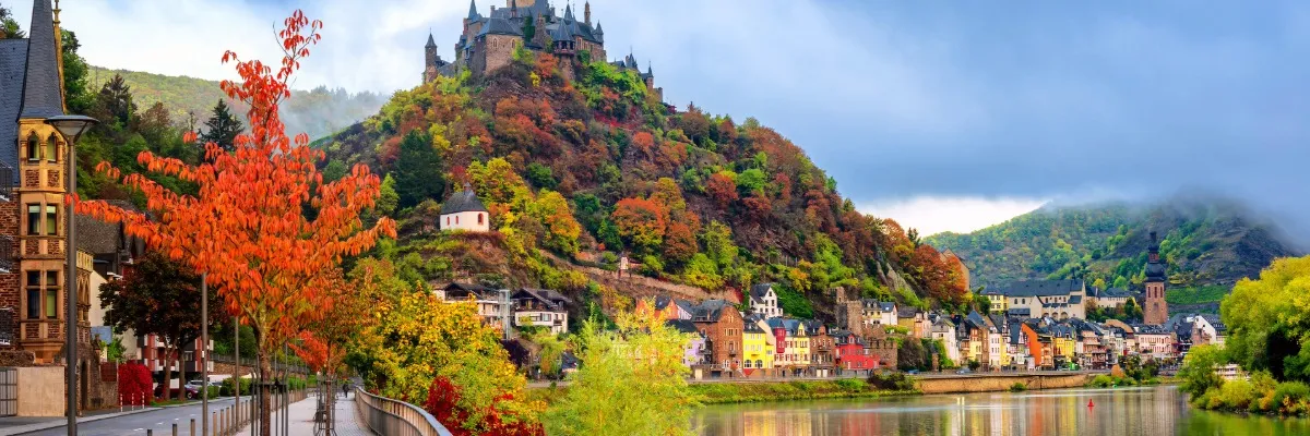 Flusskreuzfahrten in den Herbstferien Blick über die Stadt Cochem im Herbst: Bäume mit bunten Herbstblättern und Nebel.