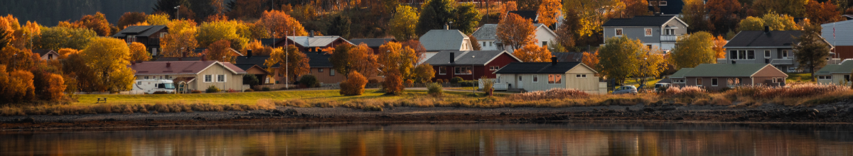 Blick über eine Stadt in Norwegen im Herbst: Bunte, mit Herbstblättern bedeckte Bäume spiegeln sich im Wasser wider.