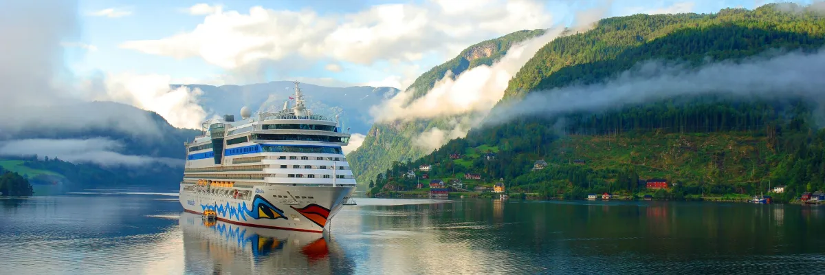 AIDA Kreuzfahrtschiff gleitet durch einen spektakulären norwegischen Fjord umgeben von grünen Berghängen und sanften Wolken.