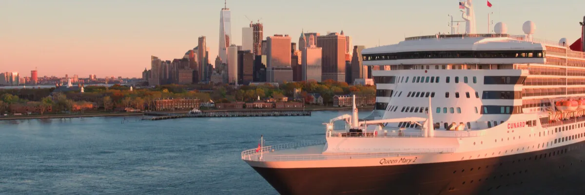 RMS Queen Mary 2: Das Cunard Flaggschiff vor der Skyline von Lower Manhattan Die RMS Queen Mary 2, der weltweit einzige und wahre Ocean Liner von Cunard, gleitet im warmen Abendlicht vor der Skyline von Manhattan und dem One World Trade Center durch den New Yorker Hafen.