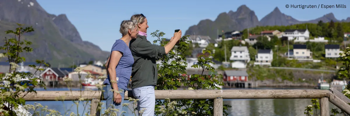 Genießen Sie extra lange Landaufenthalte bei den Hurtigruten Signature-Reisen Zwei Frauen fotografieren die wunderschöne Landschaft in Reine auf den Lofoten während einer Hurtigruten Signature Reise