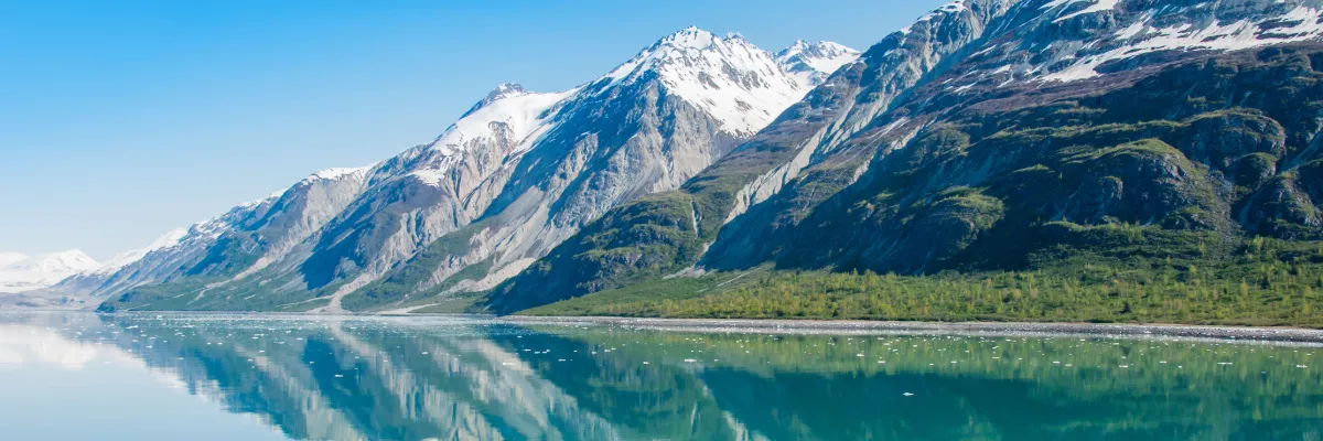 Alaska Kreuzfahrten Ein beeindruckender Gletscher in Alaska, der sich majestätisch im klaren Wasser spiegelt, umgegeben von atemberaubenden Landschaft.