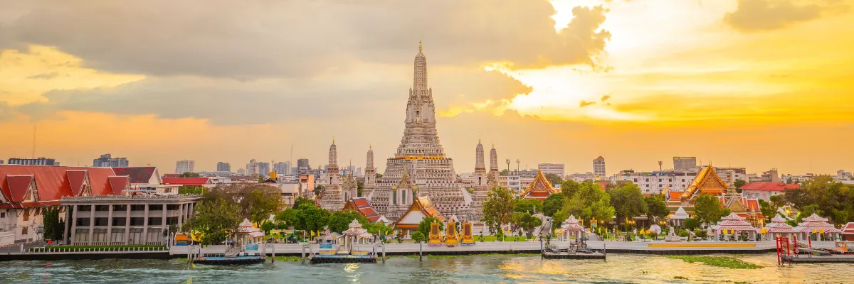Asien Reisen im Abgebot Blick auf ein wunderschönen Tempel in Bangkok, umgegeben von einer beeindruckenden Wolkenkulisse und warmen Sonnenlicht.