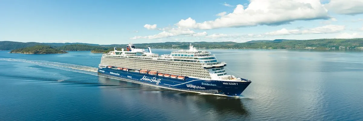 Mein Schiff 7 im Fjord Die Mein Schiff 7 fährt bei Sonnenschein durch einen norwegischen Fjord, im Hintergrund bewaldete Ufer.