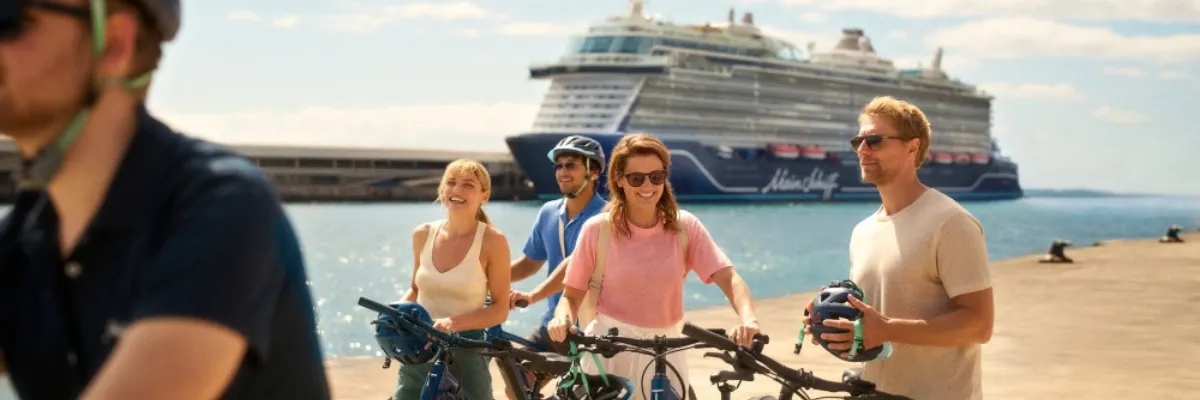 Aktiv an Land: Geführte Fahrradausflüge mit Mein Schiff® Gäste mit Fahrrädern und Helmen bei einem aktiven Fahrradausflug am Pier vor einem <em>Mein Schiff</em>® Kreuzfahrtschiff.