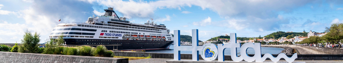 Das Kreuzfahrtschiff VASCO DA GAMA von nicko cruises vor Anker im Hafen von Horta auf der Azoreninsel Faial hinter dem markanten Horta-Schriftzug an der Uferpromenade.