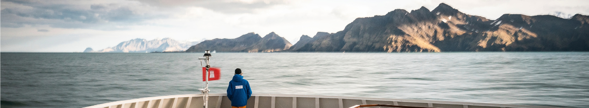 Ein Mann in einer blauen Hapag-Lloyd Expeditionsjacke steht alleine am Bug des Schiffes und genießt die Aussicht.