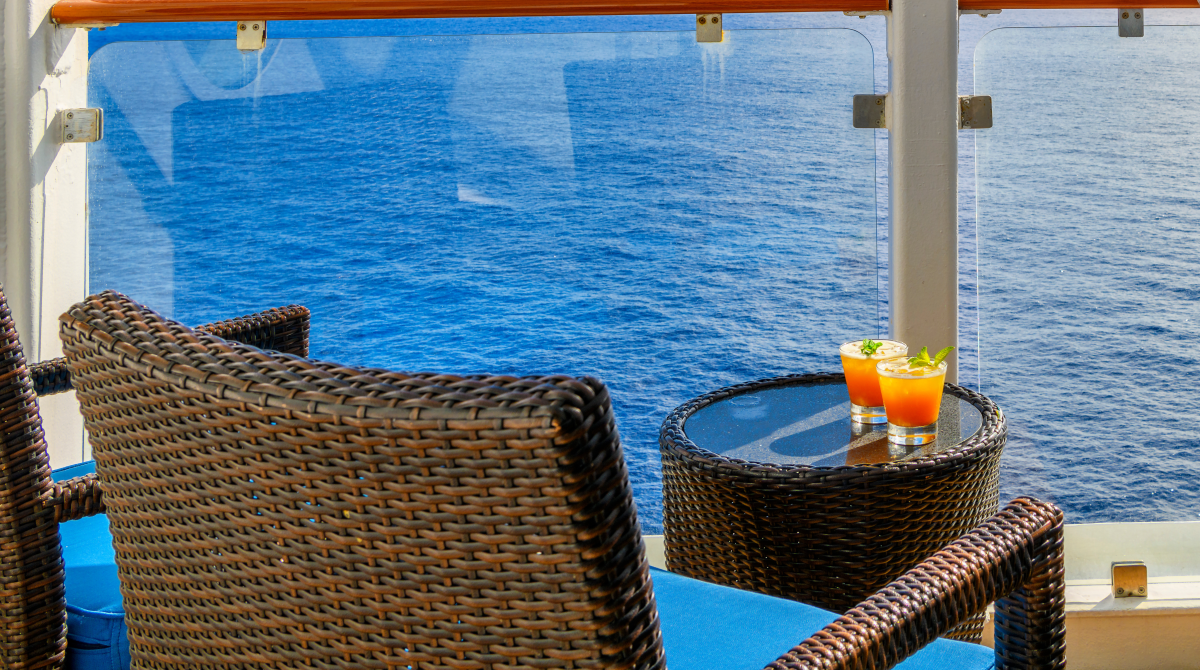 Zwei Cocktails auf einem Tisch auf einer Balkonkabine mit Glasbüstung und Blick auf das Meer.