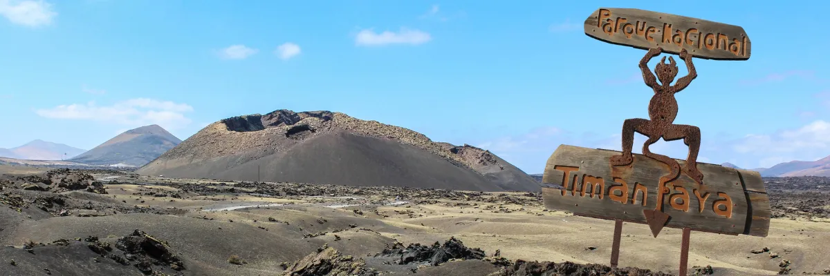 Vulkanlandschaft im Timanfaya Nationalpark auf Lanzarote. Im Vordergrund ein Schild mit einem kleinen Teufel und der Aufschrift Parque Nacional Timanfaya.