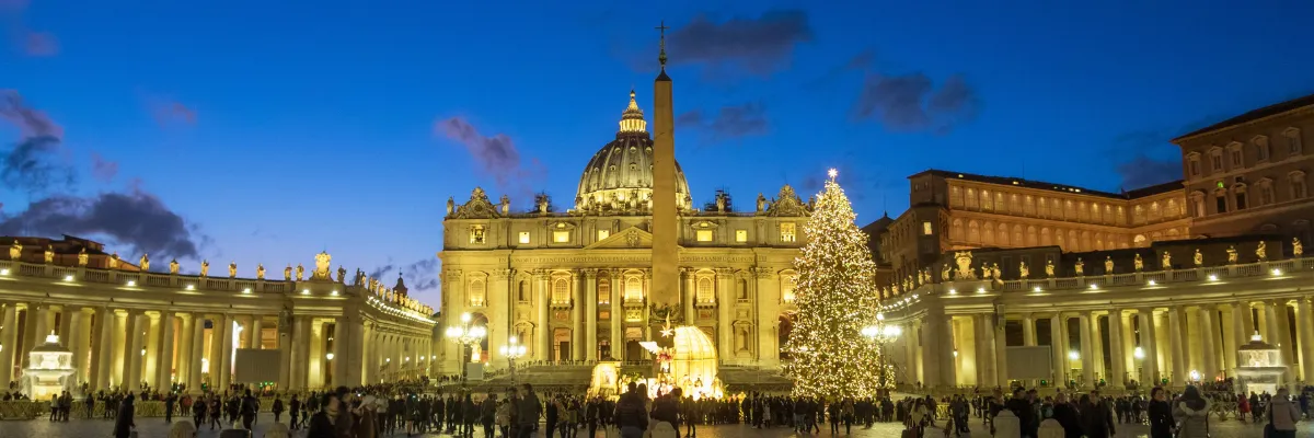 Weihnachtsbaum und Weihnachtskrippe sowie der Obelisk vor dem Petersdom in Rom im Abendlicht.