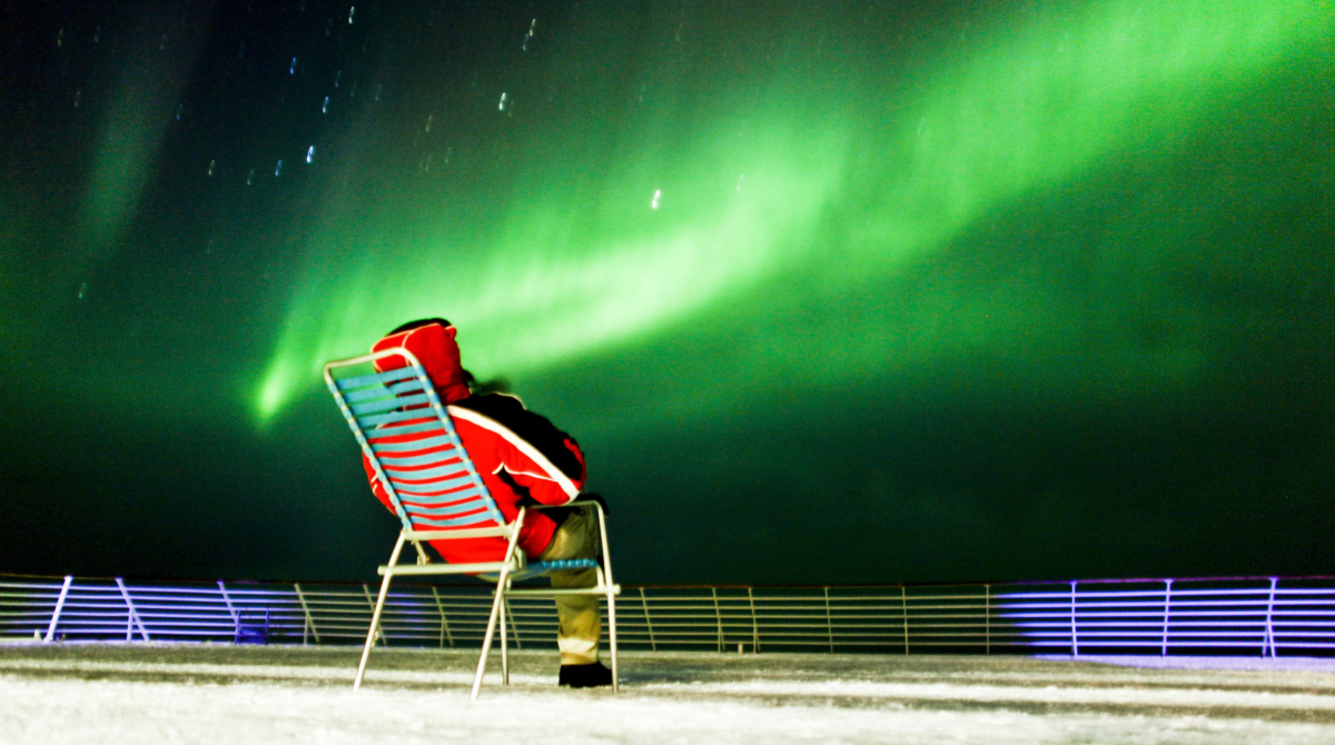 Ein Mann reist alleine auf einem Hurtigruten-Schiff und kann entspannt die Nordlichter beobachten.