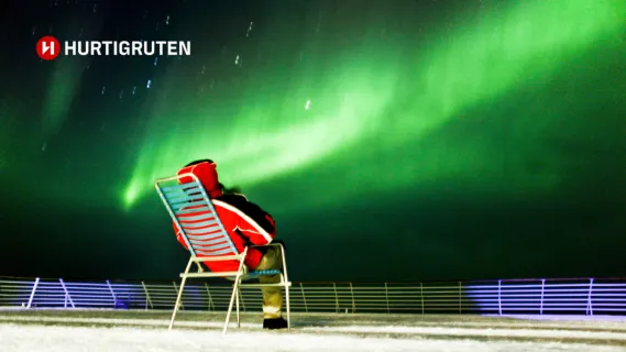 Hurtigruten Angebote für Alleinreisende ©Stein J. Bjørge / Hurtigruten Ein Mann sitzt alleine auf einem Stuhl an Deck eines Hurtigruten Schiffes und beobachtet die Nordlichter.