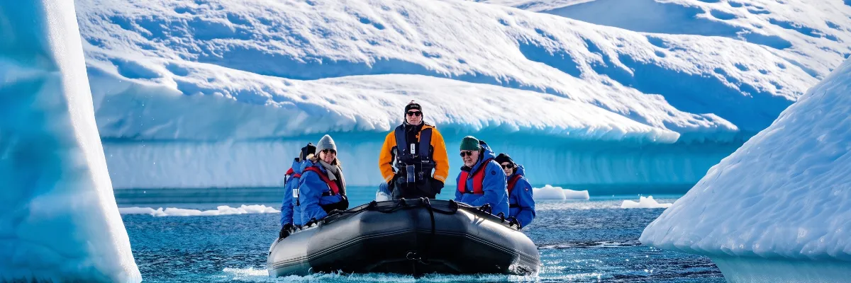 Hapag-Lloyd Cruises Zodiac-Expedition: Gäste erkunden die arktische Eiswelt Eine Gruppe von Gästen in blauer Expeditionskleidung steuert in einem wendigen Zodiac-Schlauchboot eng an majestätisch schimmernden Eisbergen und mächtigen Gletscherkulissen der Arktis entlang.