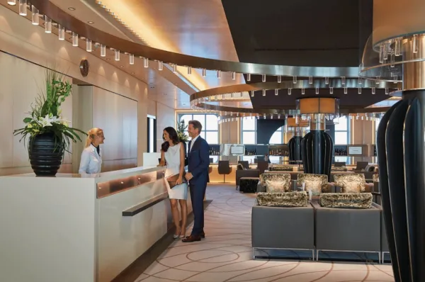 Ein Pärchen steht im Atrium an einer Rezeption und unterhält sich mit einer freundlichen und kompetenten Servicemittarbeiterin.