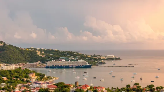 <i>Mein Schiff 3</i> vor tropischer Kulisse in malerischer Bucht Das Kreuzfahrtschiff <i>Mein Schiff 3</i> von TUI Cruises ankert vor einer grünen Küste im warmen Abendlicht.