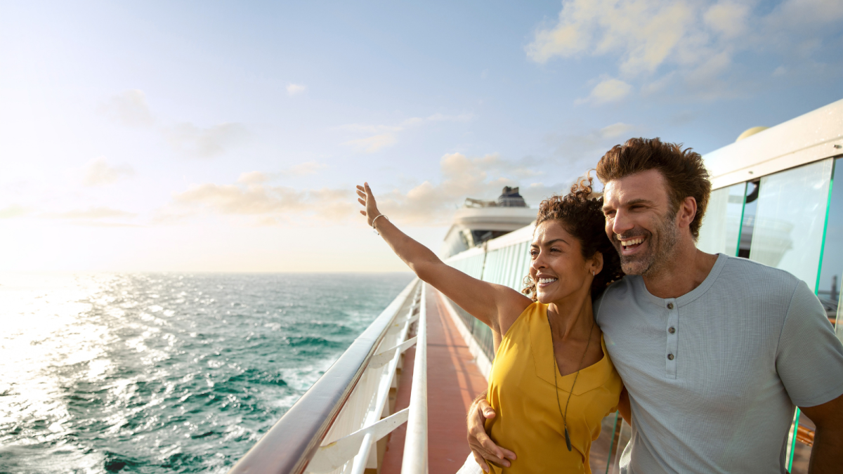 Ein lächelndes Paar steht am Balkon eines Norwegian Cruise Line Kreuzfahrtschiffs und genießt den Blick auf den sonnigen Ozean.