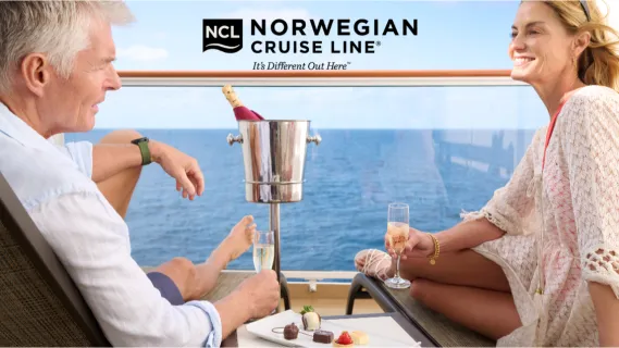 Ein Paar stößt auf dem privaten Balkon einer Norwegian Cruise Line Suite mit Champagner an und genießt den Blick auf den blauen Ozean.
