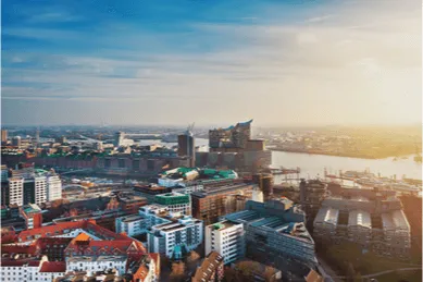 Panoramablick über den Hamburger Hafen und die HafenCity bei Sonnenuntergang. Im Zentrum des Bildes steht die markante Elbphilharmonie, während die Sonne die Stadt in ein warmes, goldenes Licht taucht.