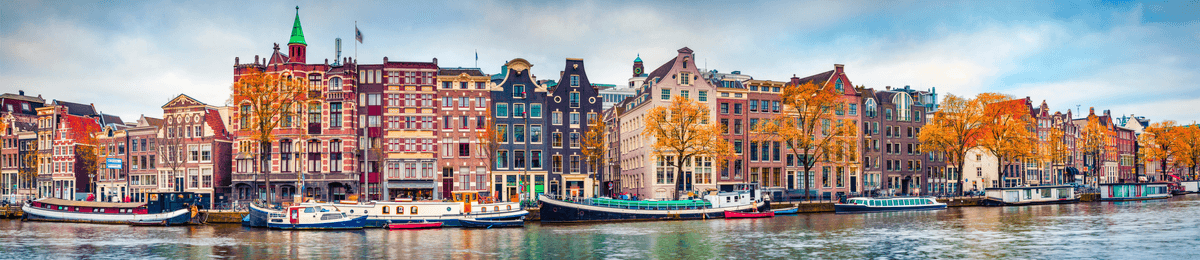 Ein Panorama einer Amsterdamer Gracht mit bunten, historischen Häusern und kleinen Booten bei bestem Wetter.