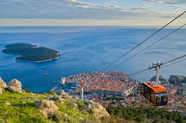 Dubrovnik in Kroatien Blick auf die Stadt Dubrovnik am Meer, von oben seilt sich eine rote Seilbahn den Berg hinunter ab.