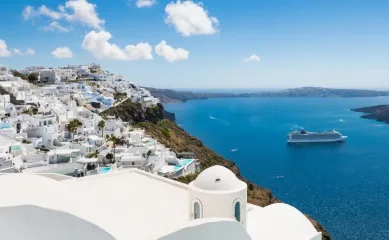 Kreuzfahrt durchs Mittelmeer Kreuzfahrtschiff auf dem türkisfarbenen Meer vor den weißen Häusern auf Santorini.