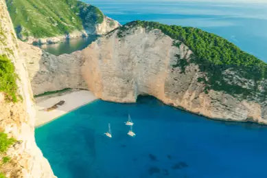 Navagio Bay aus der Luft. Links der Strand mit dem Schiffswrack, umgeben von hohen, steilen Felswänden.