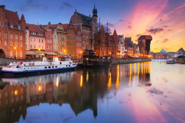 Danzig bei einer Ostsee Kreuzfahrt entdecken Die Danziger Altstadt direkt am Wasser. Boote schwimmen festgebunden im Wasser und im Hintergrund erstreckt sich ein farbenfroher Sonnenuntergang.