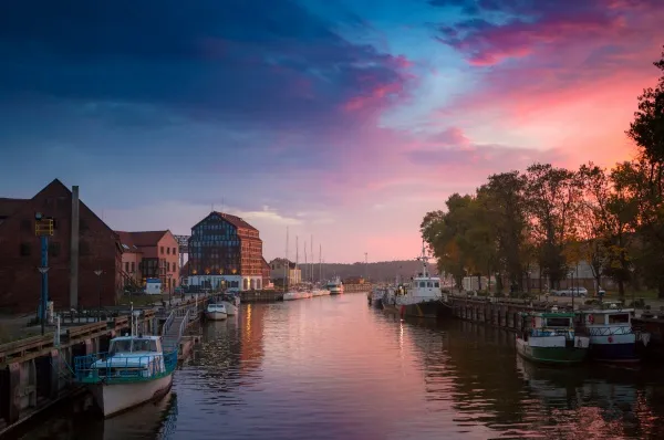 Schiff im Hafen von Klaipeda Ein Kanal in Klaipeda, Litauen an der Ostsee. Ein blau-rosaner Sonnenuntergang erstreckt sich über den Himmel und taucht die Schiffe in Bäume in sanftes Licht.