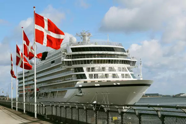 Kreuzfahrtschiff am Anleger im Hafen von Kopenhagen. Neben dem Schiff sind vier Flaggenmasten mit der dänischen Flagge zu sehen.