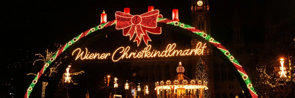 Rheinkreuzfahrten zur Adventszeit Der Eingang zum Wiener Christkindlmarkt mit einem beleuchteten Bogen und einer Schleife.