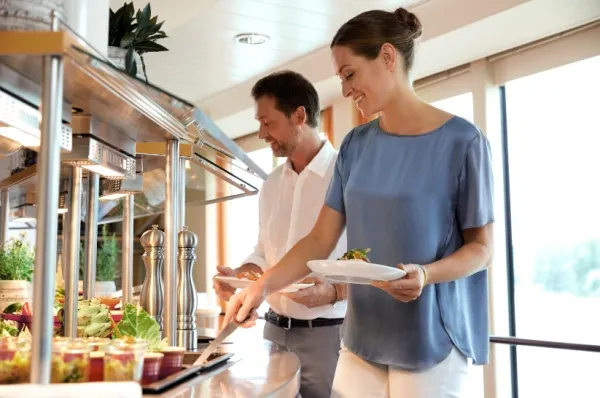 Ein Pärchen nimmt sich Essen am Buffet auf einem A-ROSA Schiff. Bei der Vollpension sind die Speisen der Buffets bereits im Preis inklusive.