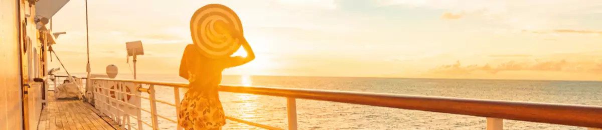 Eine junge Frau genießt an Deck eines Kreuzfahrtschiffes den Sonnenuntergang.