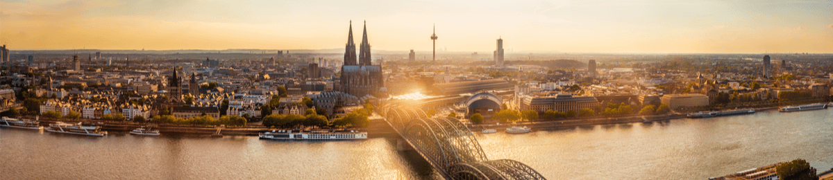 Die malerische Skyline Kölns bei Sonnenuntergang mit dem Rhein im Vordergrund.