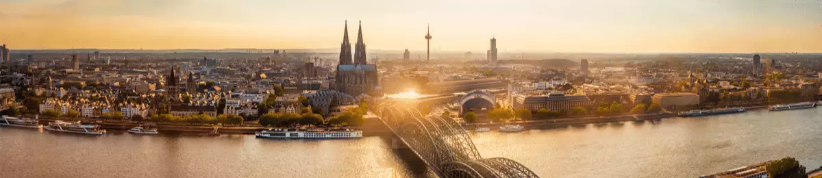 Die malerische Skyline Kölns bei Sonnenuntergang mit dem Rhein im Vordergrund.