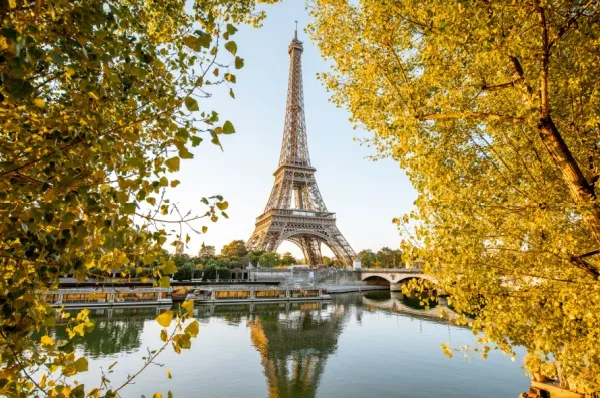 Flusskreuzfahrt Frankreich: Seine Der Eiffelturm in Paris direkt am Seine-Ufer eingerahmt von frühlingshaften Bäumen.