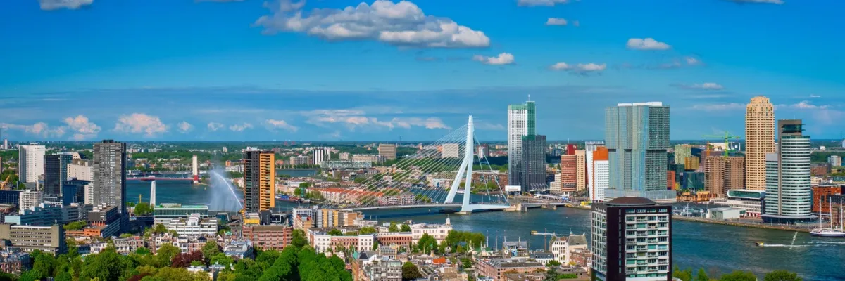 Blick über Rotterdam mit der berühmten Erasmusbrücke über die Maas. Darüber ein blauer Himmel mit einigen weißen Wolken.