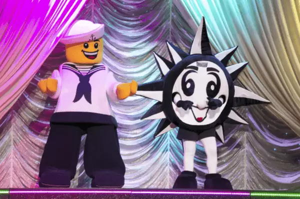 Ein LEGO Seemann und das MSC Maskottchen - ein Kompass mit Armen, Beinen und Gesicht in den Reedereifarben Blau und Weiß - stehen auf einer Bühne im Kinderbereich.