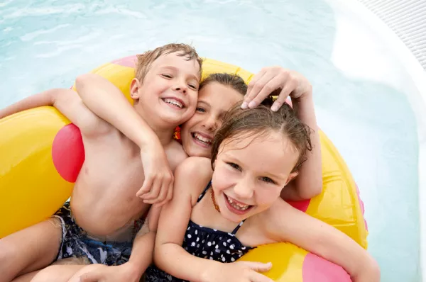 3 Kinder in einem gelben Schwimmreifen mit roten Punkten in einem Pool auf einem der A-ROSA-Schiffe.