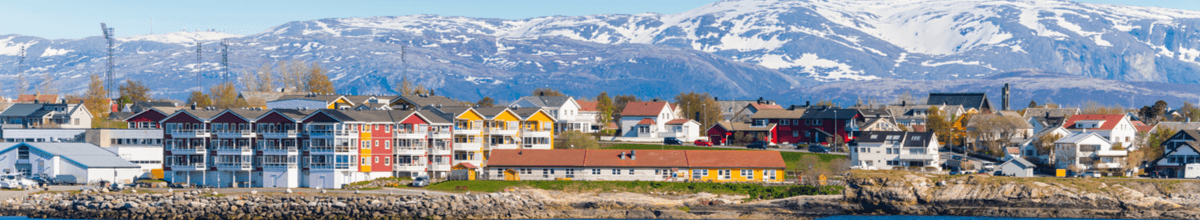 Die farbenfrohen Häuser von Bodø liegen vor einem mächtigen, schneebedeckten Gebirgszug.
