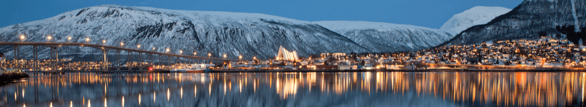 Tromsø inmitten schneebedeckter Berge. In der Bildmitte ragt die moderne Fassade der Eismeerkathedrale empor.